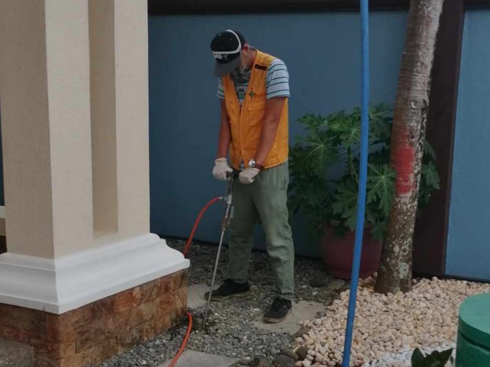 Technologist Pest Control Cebu technician using a soil injection tool on gravel near a column during site preparation.