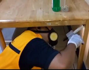 Pest control technologist in Bacolod applying treatment under a wooden table in a residential or commercial space