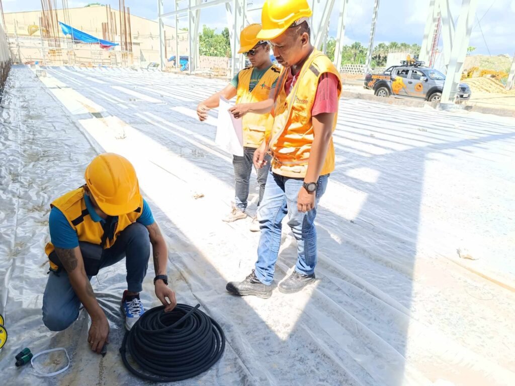 Technologist Pest Control Cebu team installing a termite reticulation system beneath a construction site using coiled hose and safety gear.